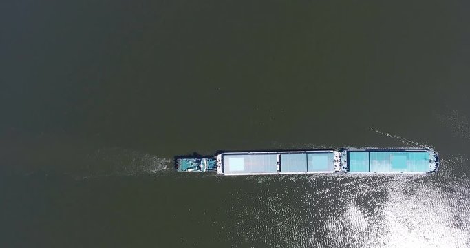 Aerial video river pusher boat transporting barge with dry cargo in middle of summer river, Central Europe