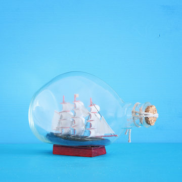nautical concept image with sail boat in the bottle over blue wooden table and background. Selective focus.