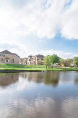 Fototapeta na wymiar Typical lakeside new-established community with newly built detached single-family homes. Cloud blue sky reflection near urban park with walking path in suburban Irving, Texas, USA