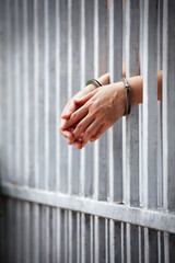 prisoner hands behind jail background.