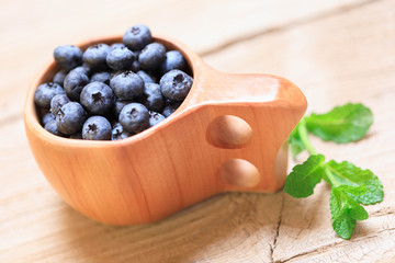 Blueberries in wooden mug Kuksa is Ancient Lapland Finnish Wooden Drinking Cup on old wooden table, close-up