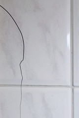 Cracked tiles on the bathroom wall need repair. Possible sign of water damage. Vertical image of building problems concept.