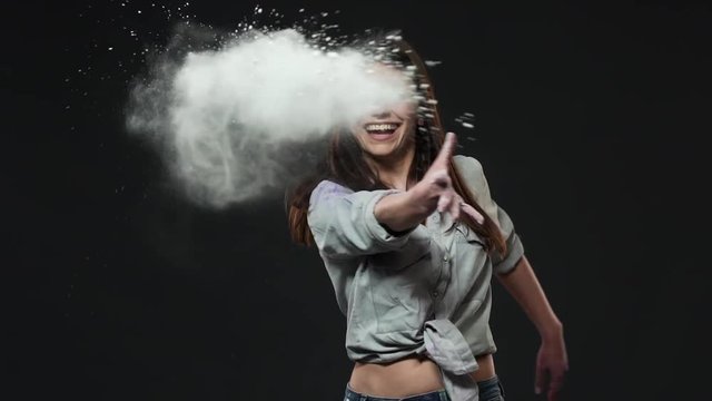 Portrait of caucasian woman throwing white paint on camera while enjoying holi festival of colors, isolated over dark gray background slow motion. Indian culture and tradition