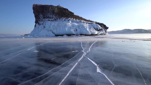 Dolly Texture Close ice Lake Baikal blue transparent deep cracks Wind gusts snow surface. Cliff mountain rock coastal splashes white. Winter cold day. Innocent untouched. Tourism. Best Russia Olkhon.