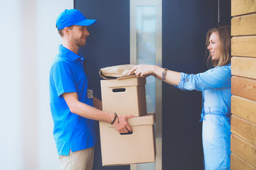 Smiling delivery man in blue uniform delivering parcel box to recipient - courier service concept....