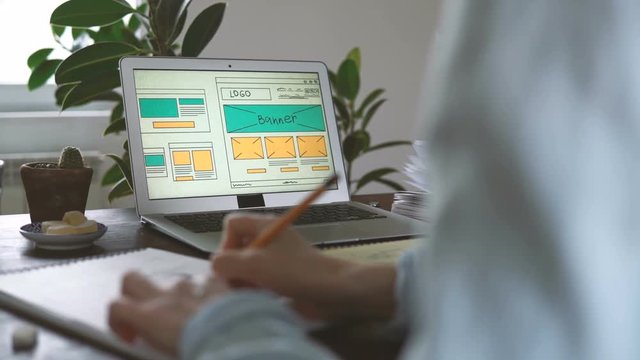 Freelancer's workplace. Web Developer makes sketches of the site in his notebook working remotely from home office