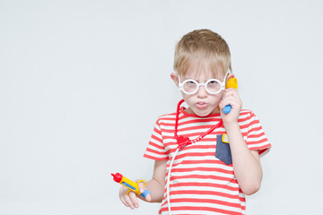 Funny boy playing doctor. Toy syringe, glasses and phonendoscope. Portrait