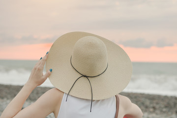 Girl in a hat sits by the sea. Back view. Close-up