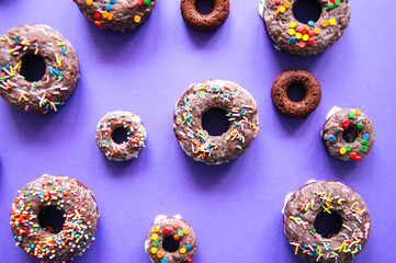Baked chocolate doughnuts with glaze and confectionary topping on a violet background. Top view.