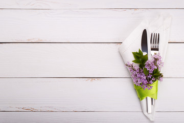 Spring festive table setting with vintage cutlery and lilac flowers on white wooden table,copy...