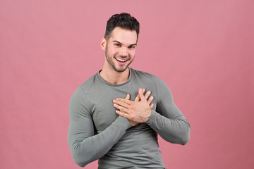 attractive young man of athletic build smiles happily and holds his hands near his heart. The concept of love, fun and intimacy.