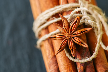 Close up of tied cinnamon sticks and anise star, Black slate background.