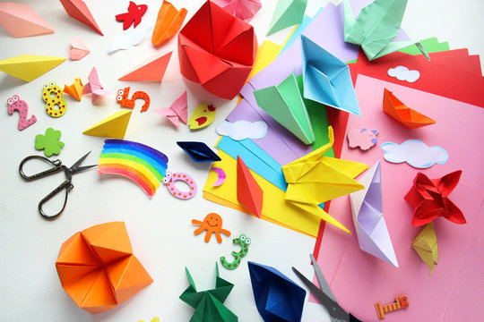 Man doing origami. Multicolored Origami and paper on  a white table.
