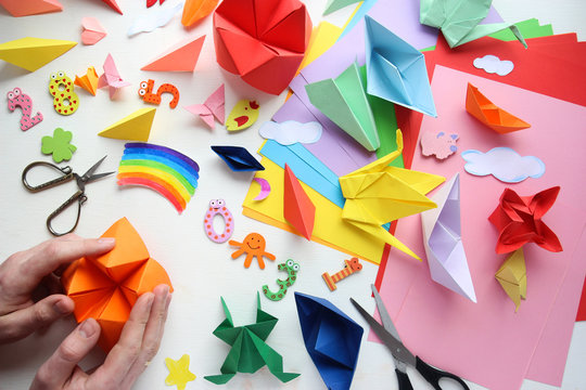 Man doing origami. Multicolored Origami and paper on  a white table.