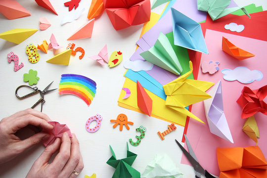 Man doing origami. Multicolored Origami and paper on  a white table.