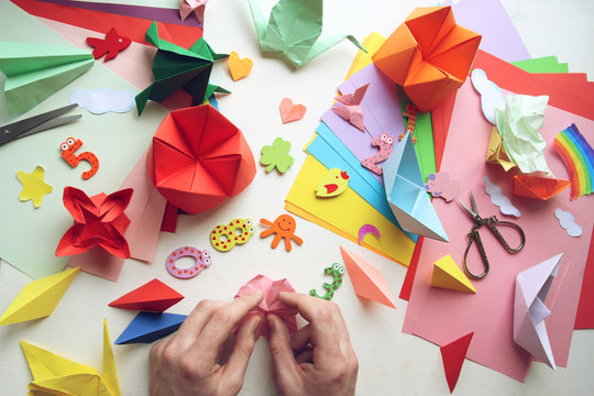 Man doing origami. Multicolored Origami and paper on  a white table.