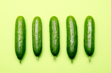 five symmetrically positioned small cucumbers on a pastel green background
