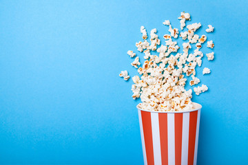 Spilled popcorn and paper bucket in red strip on blue background. Copy space for text - obrazy, fototapety, plakaty