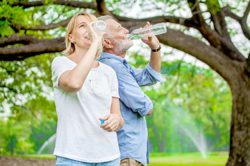Fototapeta premium Happy elderly couple enjoying drinking bottle of clean water in the park, health care concept.