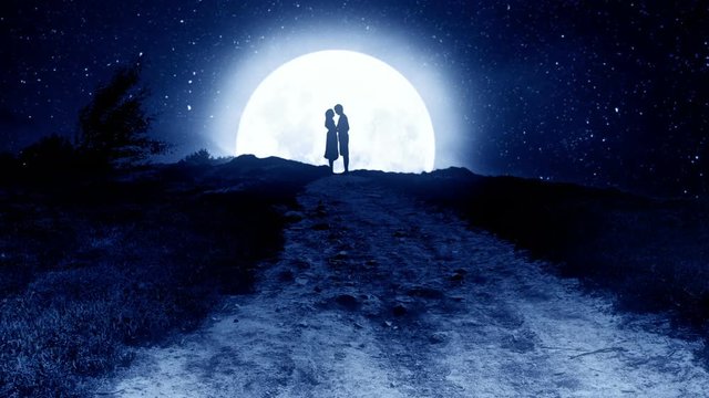 Cuddling couple on the hill at night with the moon in the background.
