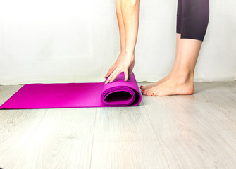 Close-up of attractive young woman folding blue yoga or fitness mat after working out at home in living room. Healthy life, keep fit concepts. Horizontal shot