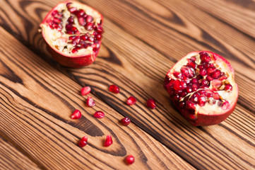 Scattered fresh ripe red seeds of pomegranate near two half pomegranate on old brown weathered wooden planks