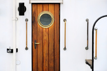 Obraz premium Vintage wooden brown door with round window on a white vessel.