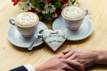 couple drinks coffee with ginger cookie in form of a heart at a cafe