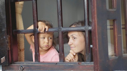 Obraz premium Mother and little daughter are looking out the window with boring emotions.