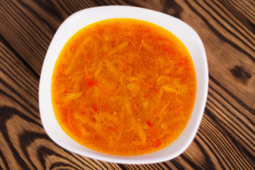 One full plate of fresh hot vegetable borscht on old weathered rustic wooden table. Top view