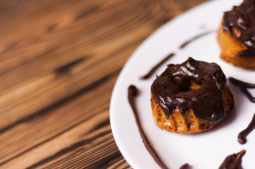 Baked cupcakes with chocolate cream on white ceramic dish on old rustic brown weathered table. Top view