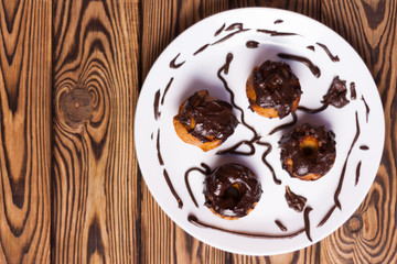 Four baked cupcakes with chocolate cream on white ceramic dish on old rustic brown weathered table. Top view