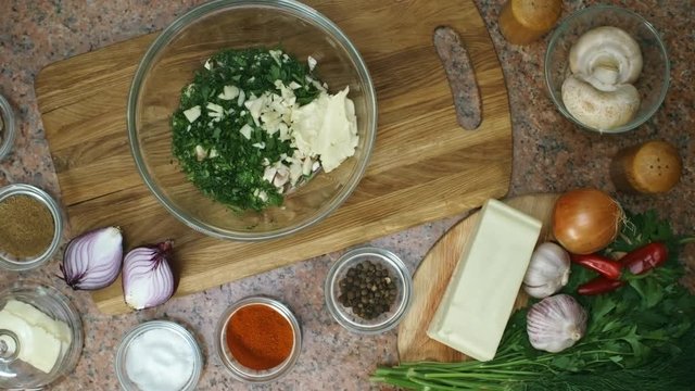 Top view of unrecognizable cook pouring water and sprinkling pepper into bowl with mix of chopped parsley, garlic and sour cream