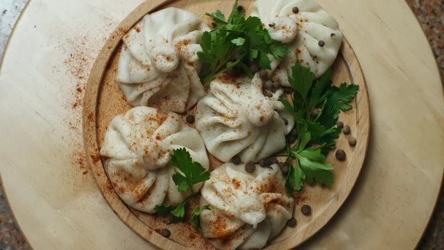 Top view of spinning wooden plate of tasty Georgian khinkali dumplings seasoned with chili pepper and decorated with fresh parsley