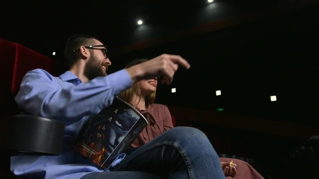 Close up of attractive young couple laughing at the movie theater. Caucasian girl and her boyfriend watching funny comedy at the cinema. Pretty female viewer tilting her head forward