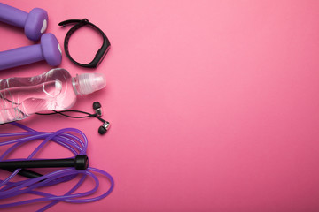 The concept of fitness - dumbbells, jump rope, fitness bracelet, headphones and water. Pink background. Copy space for text.