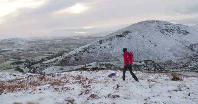 A hiker and their dog walking down a snow covered Bowscale Fell, Mungrisdale in the English Lake District, UK.