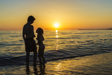Fototapeta premium Little girl and teenager bathing on a beach at sunset