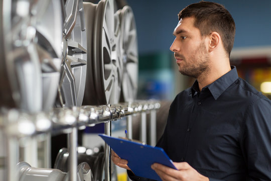 business, maintenance and people concept - male manager with alloy wheel rims and clipboard at car repair service or auto store