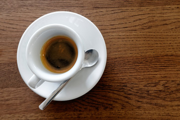 Classic italian single espresso in white cup isolated on brown wooden table from above.