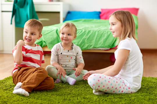 childhood, leisure and family concept - group of happy kids sitting on floor at home