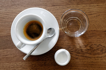 Classic italian single espresso in white cup, a milk jug and water isolated on brown wooden table from above.