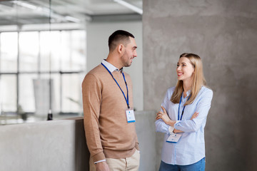 business, people and corporate concept - happy smiling man and woman with conference badges at office