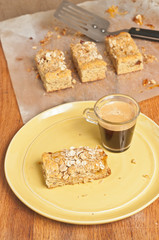 Top view of freshly baked and cut apricot, pecan bars on a yellow, round plate with glass cup of espresso, more bars cooling on parchment paper