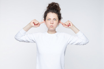Emotional young Caucasian female student in white long sleeved t-shirt grimacing, mocking, making...