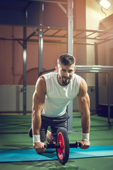Fototapeta na wymiar Muscular man doing exercises with abdominal toning wheel in gym