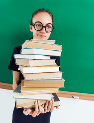 Unhappy student with stack of books near blackboard, education concept. Back to school!!