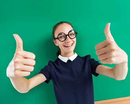 Happy young student showing her thumbs up. Photo of teen near blackboard, education concept
