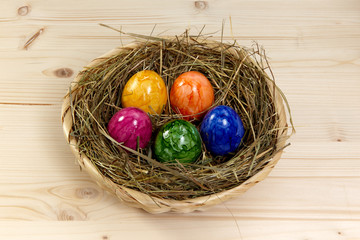 Korb mit Heu und bunten Eiern auf Holz aus Fichte