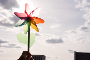 Rainbow coloured pinwheel held up against cloudy sky with sun shining though.